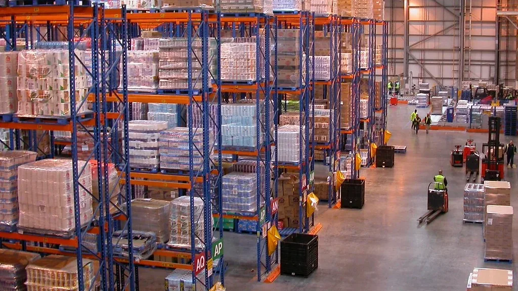 Interior of a large commercial warehouse with high storage racks and active aisles.